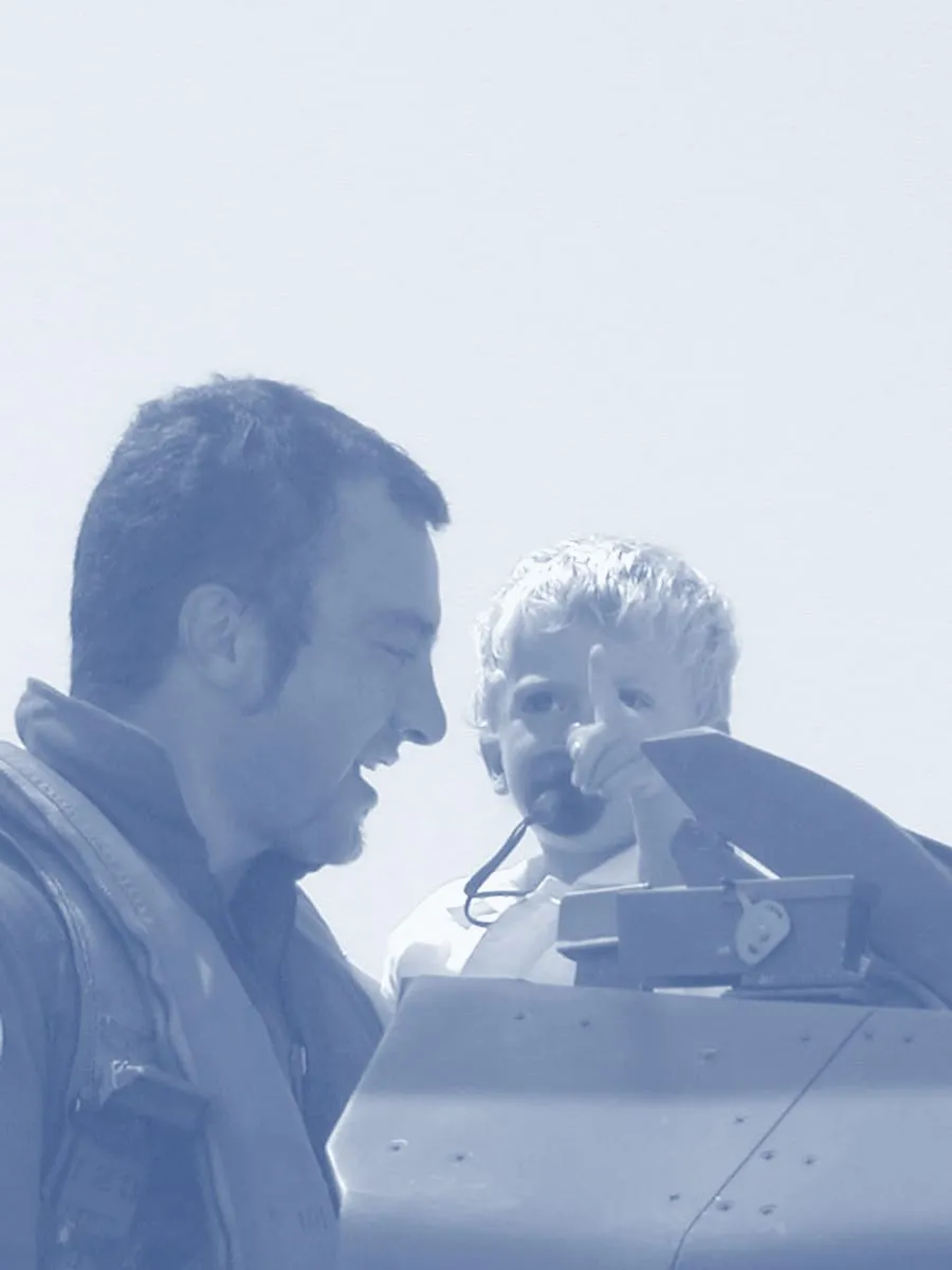 Fabio Masci da giovane, in tuta di volo, ride con il figlio piccolo seduto nell'abitacolo di un F-16 che indica davanti a sé
